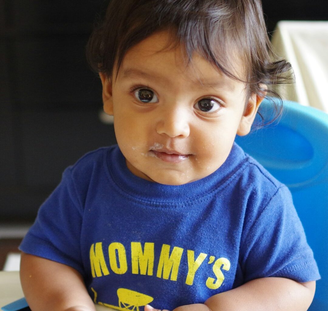 A baby in a blue shirt with yellow text.