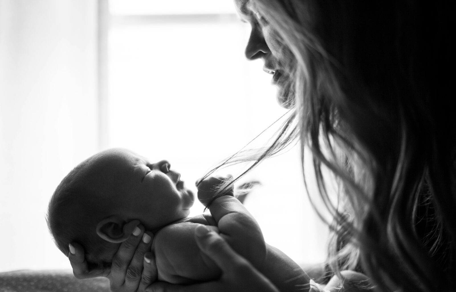 Moeder zit vermoeid met haar baby op de arm bij het raam