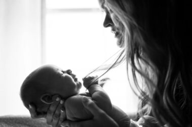 Moeder zit vermoeid met haar baby op de arm bij het raam