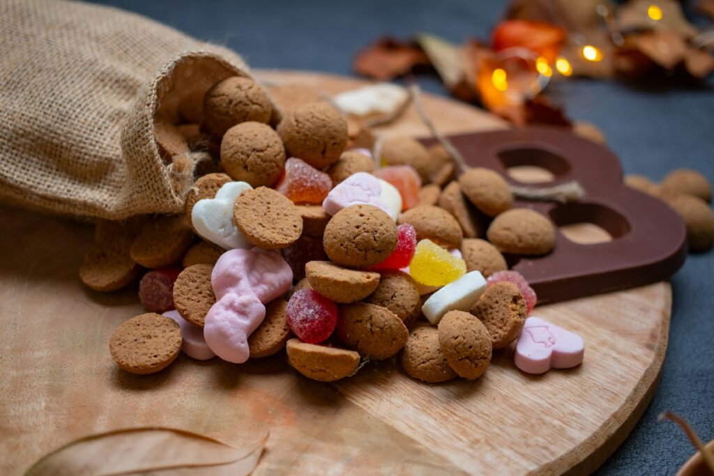 Pepernoten en snoepgoed uit een jutezak op een houten plank, met een chocoladeletter ernaast