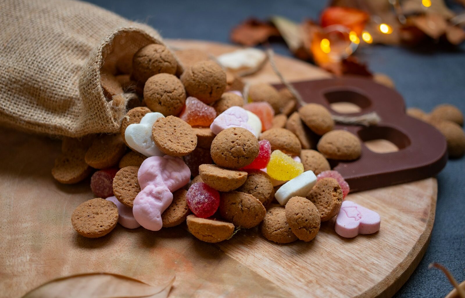 Pepernoten en snoepgoed uit een jutezak op een houten plank, met een chocoladeletter ernaast