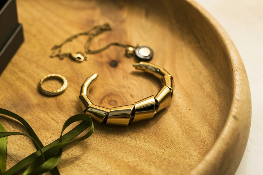 Een gouden armband, een ring en een fijn kettinkje op een houten schaaltje