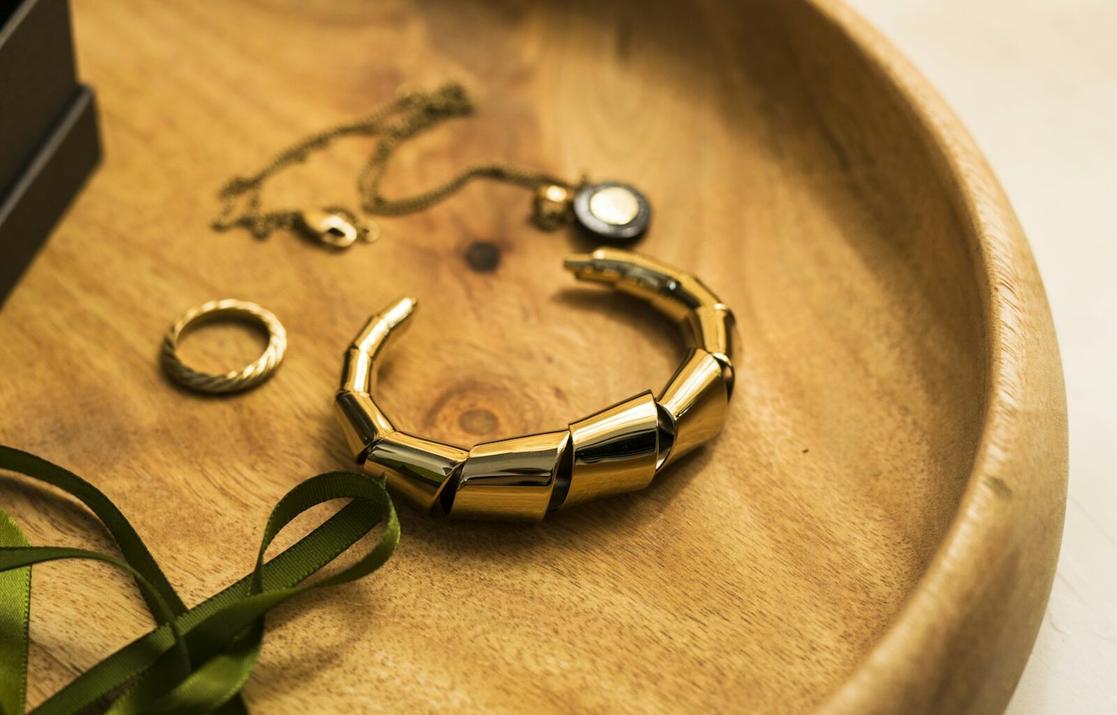 Een gouden armband, een ring en een fijn kettinkje op een houten schaaltje