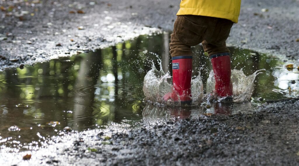Kinderen in regenlaarzen springen in een plas in het herfstbos