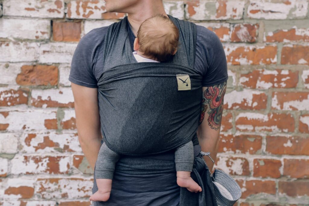 Ouder draagt een baby in een donkere draagdoek