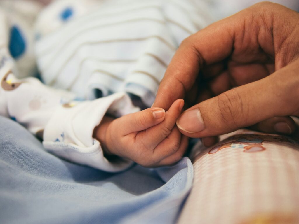 Hand van een ouder die de kleine hand van een pasgeboren baby vasthoudt
