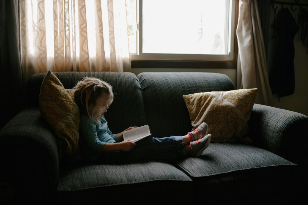 Kind van een jaar of tien leest alleen een boek op de bank in de woonkamer