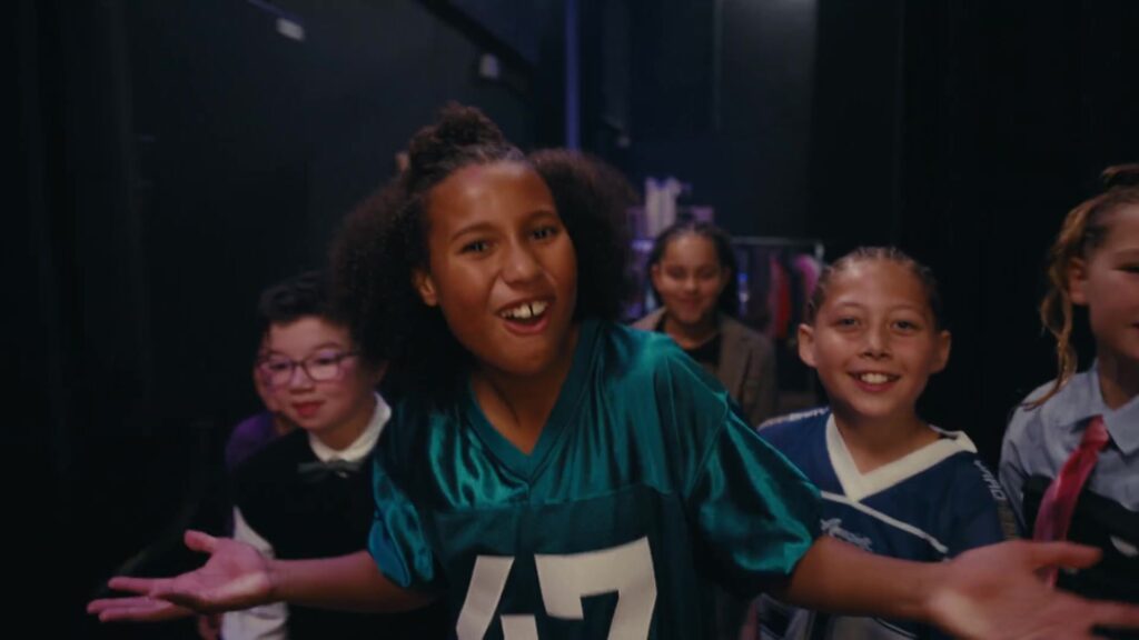 Kinderen van Kinderen voor Kinderen lopen achter de schermen naar het podium in de clip Spot aan