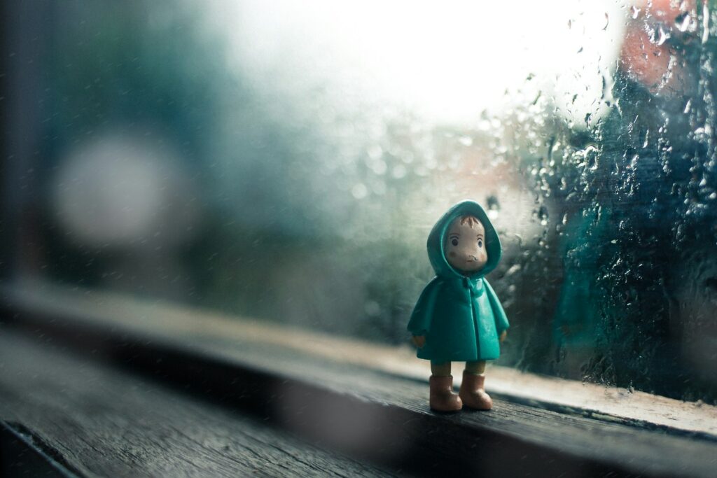 Kind kijkt vanuit huis door een raam naar storm en regen
