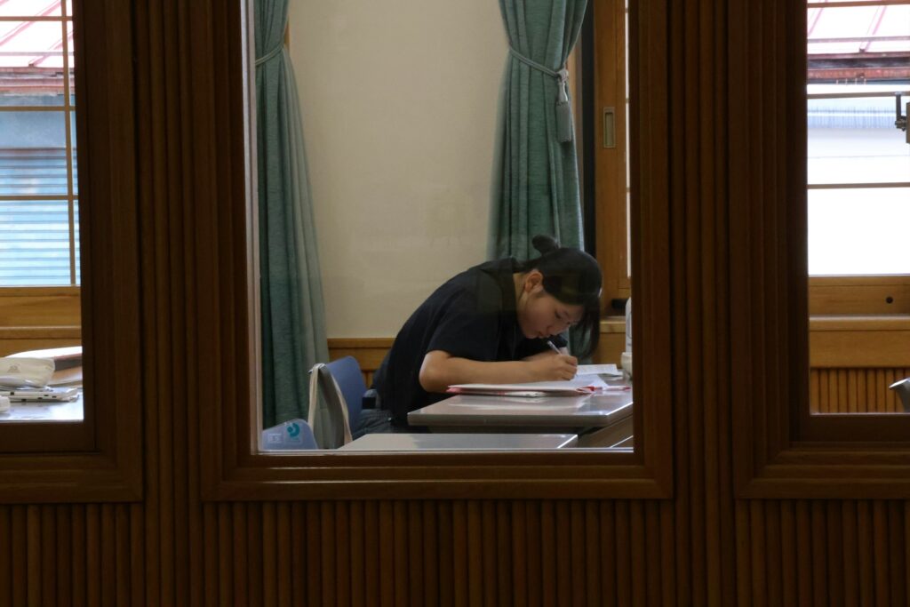Dromerig schoolkind kijkt uit het raam terwijl het huiswerk voor hem op tafel ligt